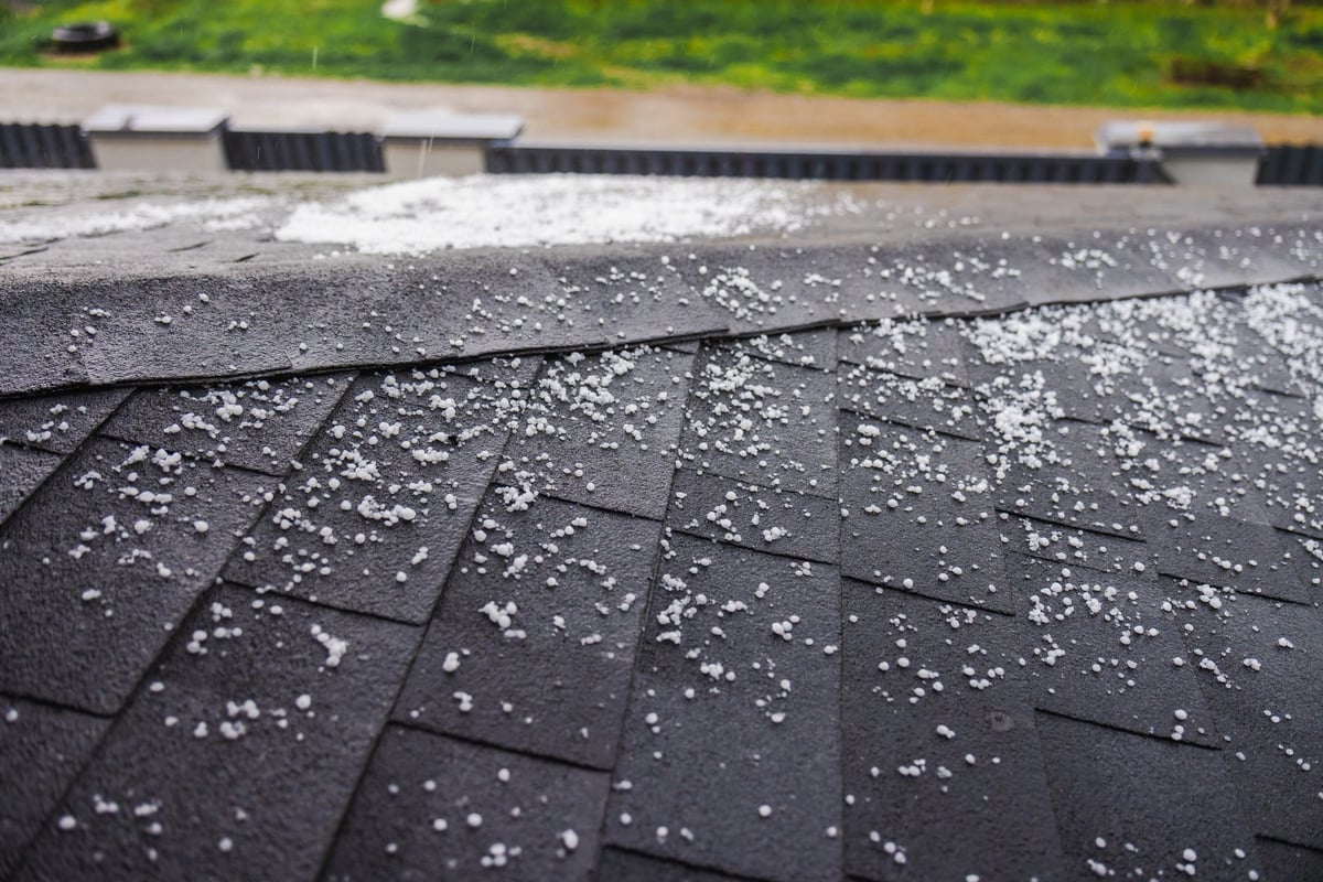 Dark shingled roof covered with hailstones following a severe hailstorm